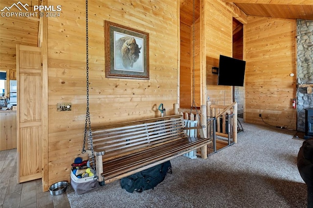 interior space with high vaulted ceiling, carpet flooring, and wooden walls