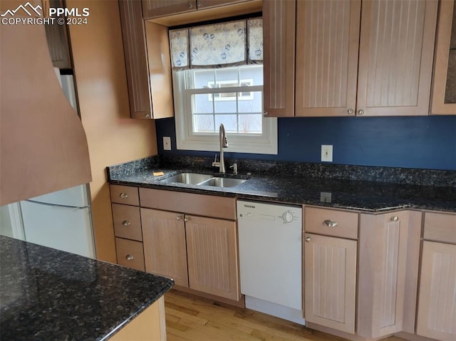 kitchen with dishwasher, sink, light wood-type flooring, and dark stone counters