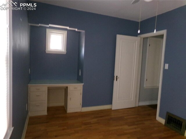 unfurnished bedroom with built in desk, wood-type flooring, and ceiling fan