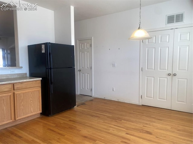 kitchen with black fridge, hanging light fixtures, and light wood-type flooring