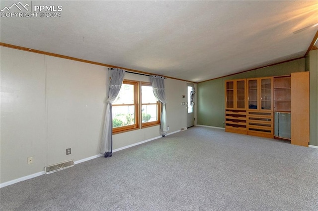 carpeted spare room featuring a textured ceiling, vaulted ceiling, and crown molding