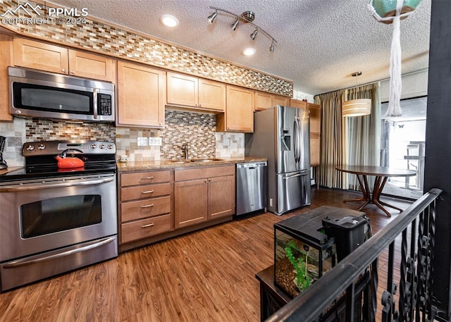 kitchen featuring appliances with stainless steel finishes, backsplash, rail lighting, dark hardwood / wood-style floors, and pendant lighting