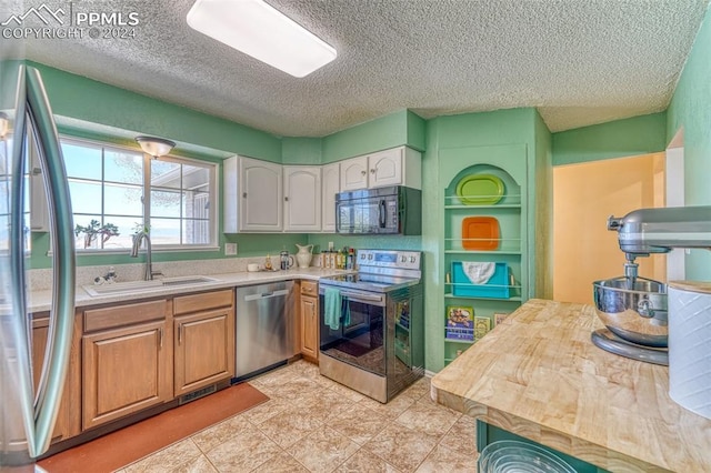 kitchen featuring white cabinetry, sink, stainless steel appliances, wooden counters, and a textured ceiling