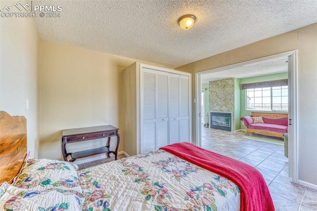 bedroom with a large fireplace, light tile patterned floors, a textured ceiling, and a closet