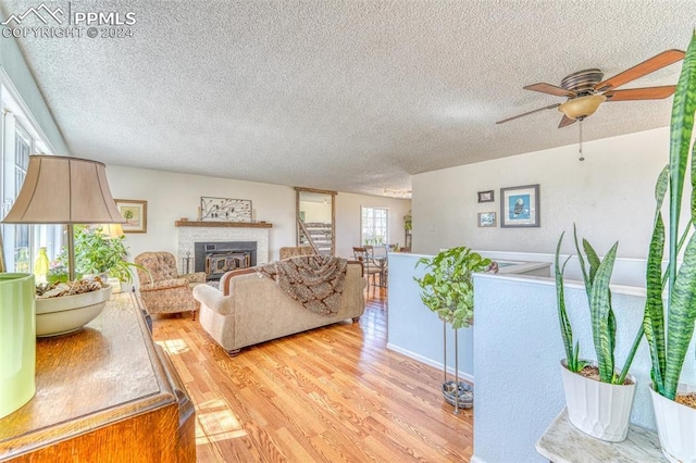 living room with ceiling fan, a fireplace, a textured ceiling, and light wood-type flooring