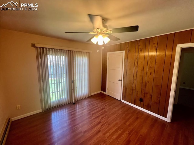 unfurnished bedroom featuring dark hardwood / wood-style flooring, ceiling fan, wooden walls, and a baseboard heating unit