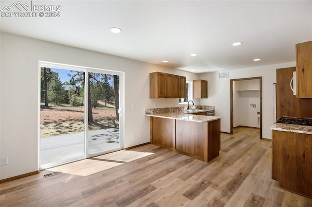 kitchen with light wood-type flooring, kitchen peninsula, light stone counters, and sink