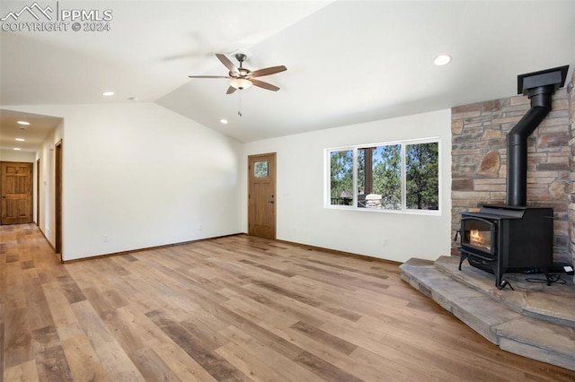 unfurnished living room featuring vaulted ceiling, ceiling fan, a wood stove, and light hardwood / wood-style flooring