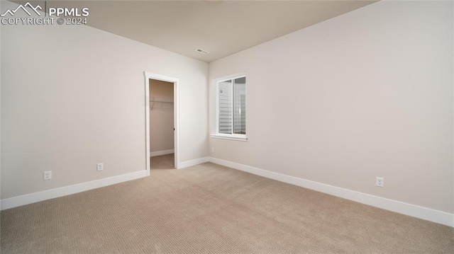 unfurnished bedroom with a spacious closet, a closet, and light carpet