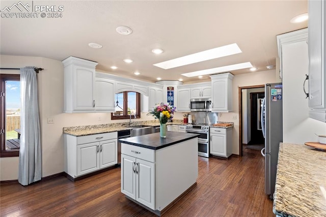 kitchen with a skylight, white cabinetry, stainless steel appliances, and dark hardwood / wood-style floors