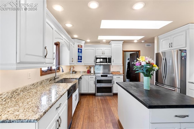 kitchen with a skylight, appliances with stainless steel finishes, a center island, white cabinets, and hardwood / wood-style floors