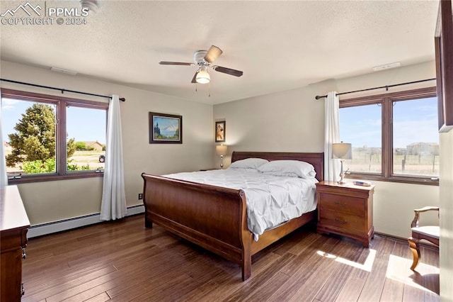 bedroom featuring a baseboard heating unit, ceiling fan, dark hardwood / wood-style floors, and multiple windows