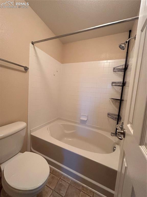 bathroom with tile patterned floors, tiled shower / bath combo, toilet, and a textured ceiling