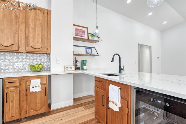 kitchen with light stone countertops, light hardwood / wood-style floors, sink, beverage cooler, and pendant lighting