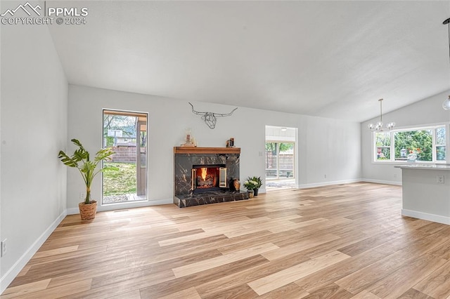 unfurnished living room with lofted ceiling, a high end fireplace, light wood-type flooring, and an inviting chandelier