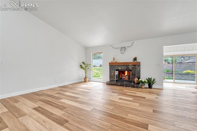 unfurnished living room with light wood-type flooring, a high end fireplace, and vaulted ceiling