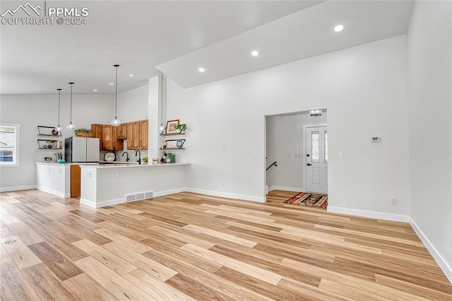 unfurnished living room with high vaulted ceiling, plenty of natural light, and light hardwood / wood-style floors