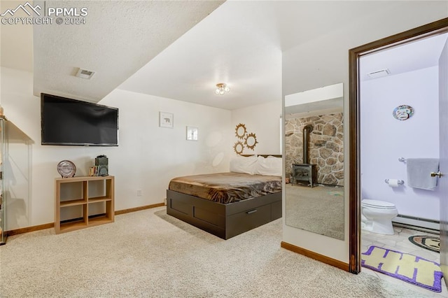 bedroom with carpet floors, a textured ceiling, a wood stove, a baseboard heating unit, and connected bathroom