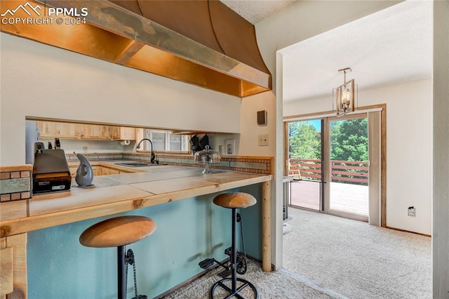 kitchen featuring a kitchen breakfast bar, hanging light fixtures, light carpet, kitchen peninsula, and sink