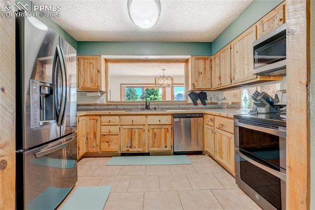 kitchen with a textured ceiling, appliances with stainless steel finishes, a notable chandelier, sink, and light tile flooring