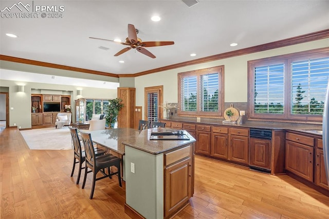 kitchen with a breakfast bar, a center island, dark stone counters, ceiling fan, and ornamental molding