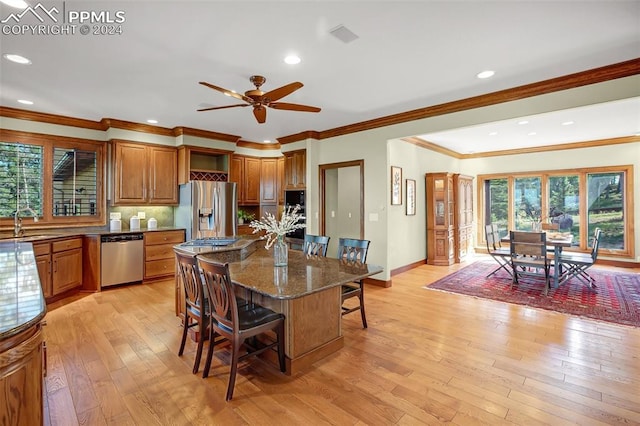 kitchen featuring stainless steel appliances, crown molding, dark stone countertops, light hardwood / wood-style floors, and a breakfast bar area