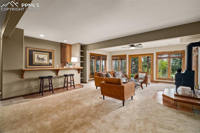 carpeted living room with built in shelves, ceiling fan, and a wood stove