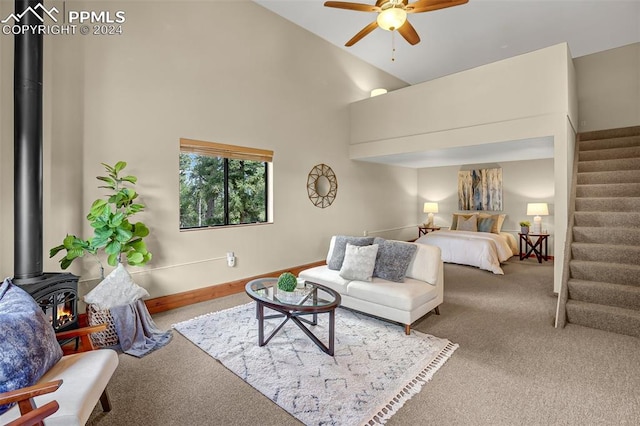 bedroom with carpet flooring, a wood stove, ceiling fan, and a high ceiling