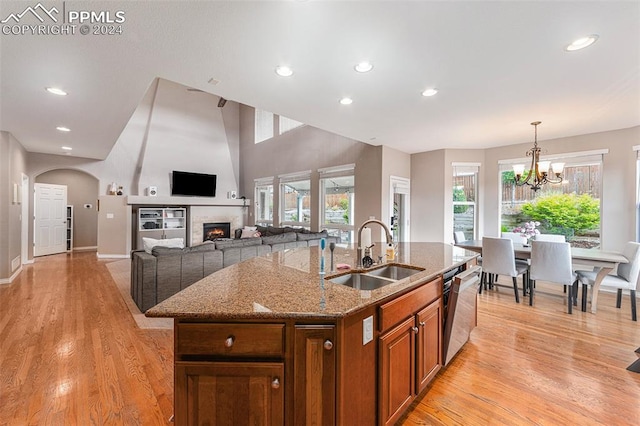 kitchen with a kitchen island with sink, light hardwood / wood-style floors, light stone countertops, sink, and a notable chandelier