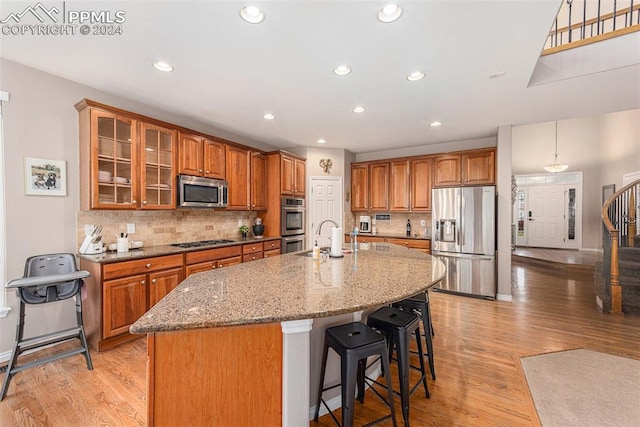 kitchen with light wood-type flooring, decorative backsplash, a kitchen island with sink, sink, and stainless steel appliances