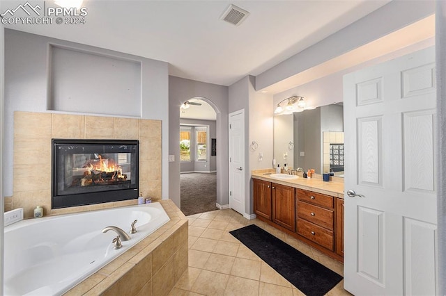 bathroom with tile patterned flooring, vanity, a relaxing tiled tub, and a tiled fireplace