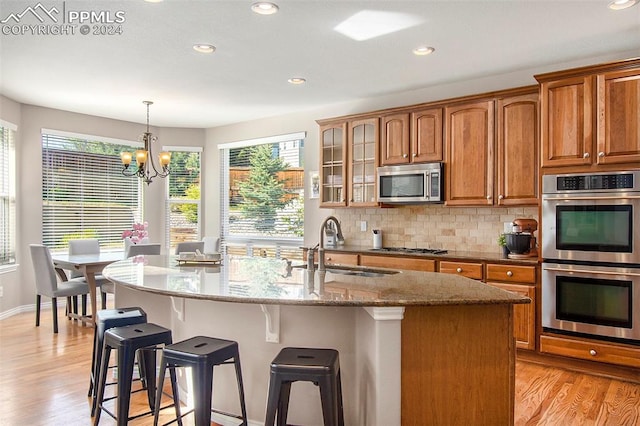 kitchen featuring a kitchen island with sink, appliances with stainless steel finishes, light stone counters, and light hardwood / wood-style floors