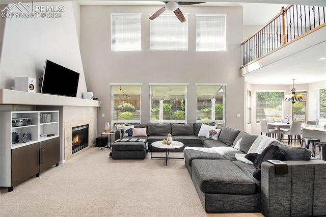 living room with a tiled fireplace, ceiling fan with notable chandelier, a towering ceiling, and light carpet