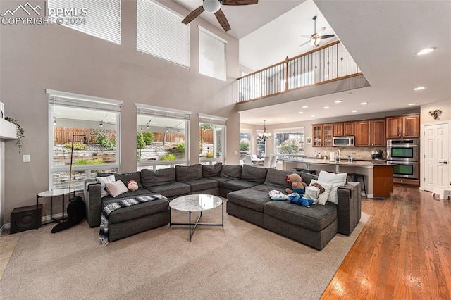 living room with hardwood / wood-style flooring, a towering ceiling, and ceiling fan