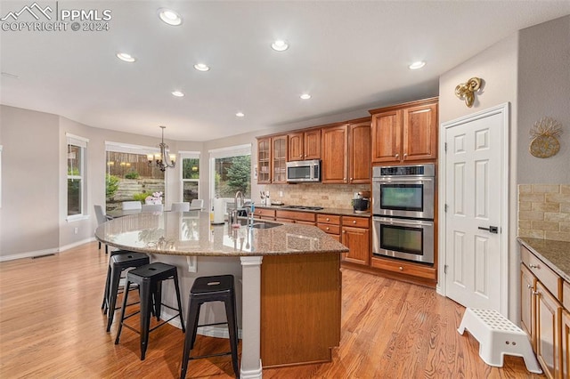 kitchen featuring sink, light wood-type flooring, appliances with stainless steel finishes, decorative backsplash, and a kitchen island with sink