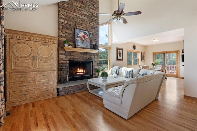 living room featuring light wood-type flooring, ceiling fan, a stone fireplace, and high vaulted ceiling