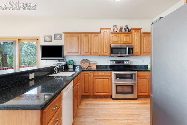 kitchen featuring stainless steel appliances, dark stone countertops, light hardwood / wood-style flooring, and sink