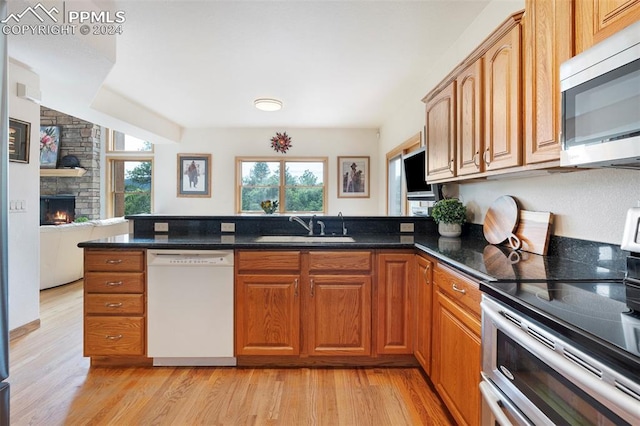 kitchen with dark stone countertops, sink, light wood-type flooring, appliances with stainless steel finishes, and a stone fireplace