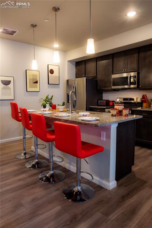 kitchen featuring dark brown cabinetry, dark hardwood / wood-style flooring, hanging light fixtures, an island with sink, and appliances with stainless steel finishes