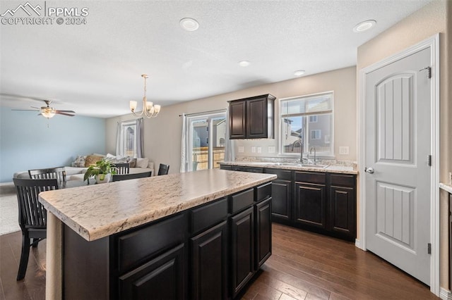 kitchen featuring dark wood-type flooring, a kitchen island, ceiling fan with notable chandelier, pendant lighting, and sink