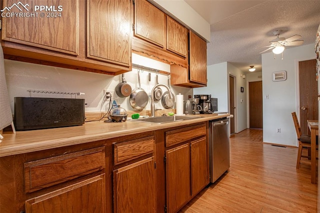 kitchen featuring a textured ceiling, sink, ceiling fan, stainless steel dishwasher, and light hardwood / wood-style floors