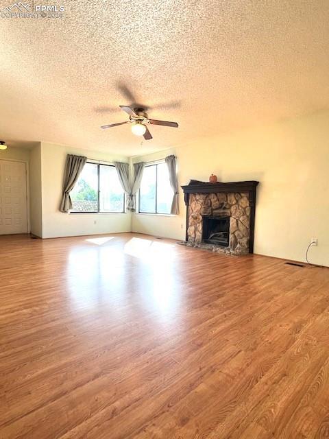 unfurnished living room featuring a textured ceiling, ceiling fan, a stone fireplace, and hardwood / wood-style flooring