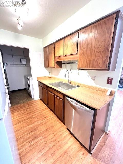 kitchen featuring dishwasher, sink, washer and clothes dryer, and light hardwood / wood-style flooring