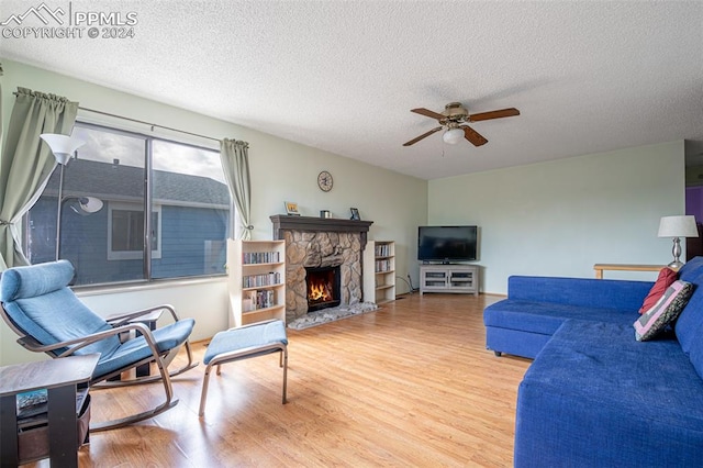 living room with ceiling fan, a fireplace, wood-type flooring, and a textured ceiling