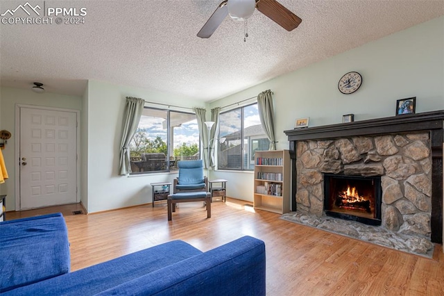 living room featuring ceiling fan, a fireplace, a textured ceiling, and light hardwood / wood-style flooring