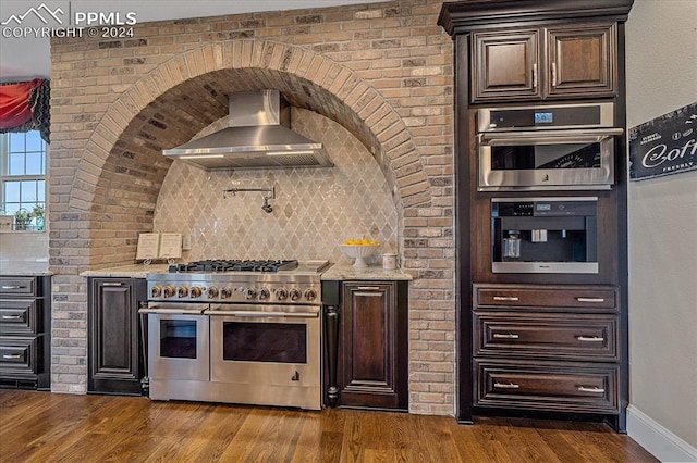 kitchen featuring stainless steel appliances, wood-type flooring, wall chimney exhaust hood, and backsplash