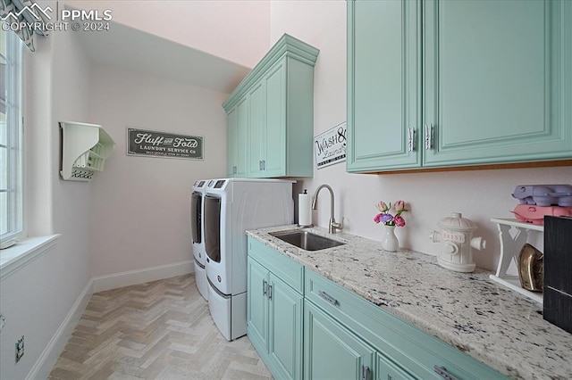 clothes washing area featuring light parquet floors, sink, washer and clothes dryer, and cabinets