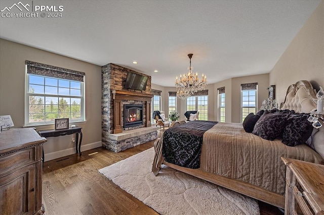 bedroom with a notable chandelier, hardwood / wood-style floors, a stone fireplace, and multiple windows