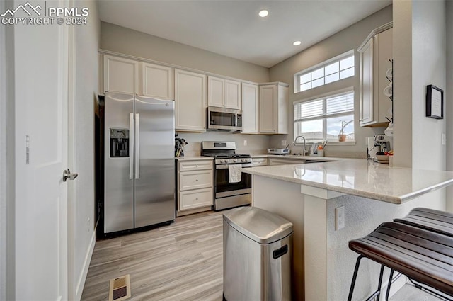 kitchen featuring white cabinets, a breakfast bar area, light hardwood / wood-style floors, kitchen peninsula, and stainless steel appliances