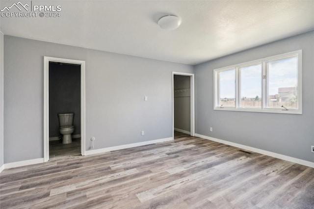 unfurnished bedroom featuring connected bathroom, light wood-type flooring, and a closet